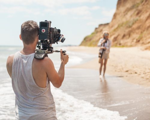 Professional videographer- film maker filming music clip on sand coast - beach near sea.