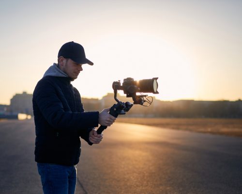 Young man filming with camera and gimbal. Filmmaker standing against city at sunrise. Prague, Czech